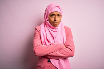 Young African American afro woman wearing muslim hijab over isolated pink background skeptic and nervous, disapproving expression on face with crossed arms. Negative person.