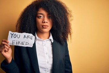 African american business boss woman with afro hair holding you are fired paper for dismissal with a confident expression on smart face thinking serious