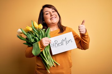 Beautiful plus size woman celebrating mothers day holding best mom message and tulips happy with big smile doing ok sign, thumb up with fingers, excellent sign