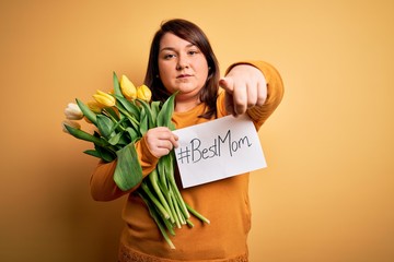 Beautiful plus size woman celebrating mothers day holding best mom message and tulips pointing with finger to the camera and to you, hand sign, positive and confident gesture from the front