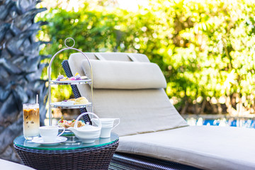 Afternoon tea set with latte coffee and hot tea on table neary chair around swimming pool