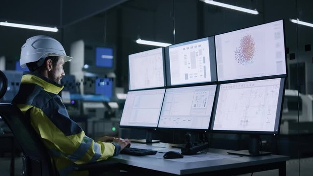 Industry 4.0 Modern Factory: Facility Operator Controls Workshop Production Line, Uses Computer with Screens Showing Complex UI of Machine Operation Processes, Controllers, Machinery Blueprints