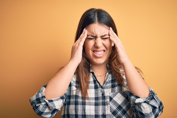 Young beautiful woman wearing casual shirt standing over isolated orange background suffering from headache desperate and stressed because pain and migraine. Hands on head.