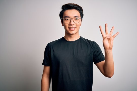 Young handsome chinese man wearing black t-shirt and glasses over white background showing and pointing up with fingers number four while smiling confident and happy.
