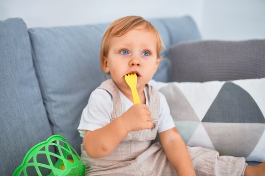 Adorable blonde toddler sitting on the sofa playing with plastic meals toys at home