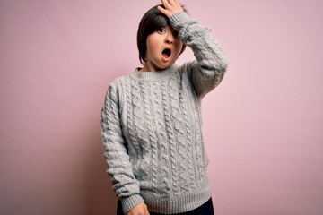 Young down syndrome woman wearing casual sweater over isolated background surprised with hand on...