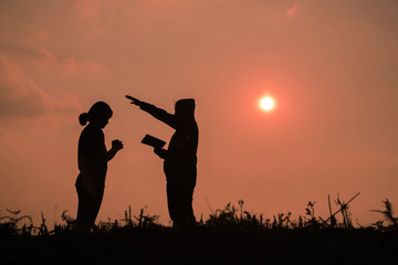 Fototapeta na wymiar Silhouette of two teen girls praying to god with the bible.