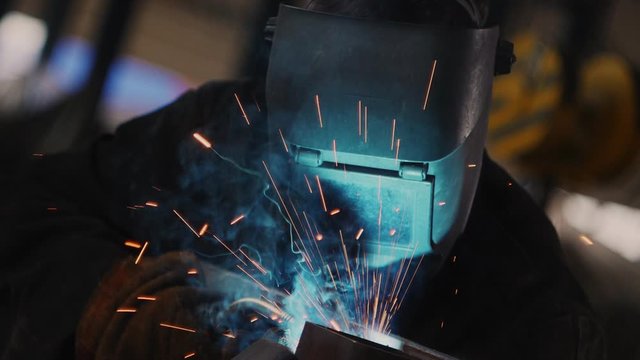welder in special mask connects metal parts at bright sparks
