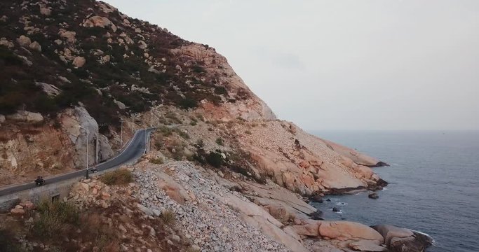 following three bikers from behind driving on a scenic road carved in cliff on seaside in Phan Rhang, Vietnam