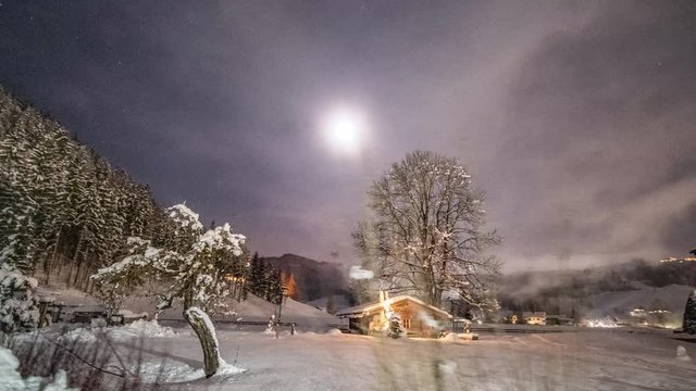 Winter fairy tale in a small village Altenmarkt im Pongau. The thick blanket of snow on the ground, snow-covered trees, and houses. Bright festive lights and the cottage. Full moon on the dark sky