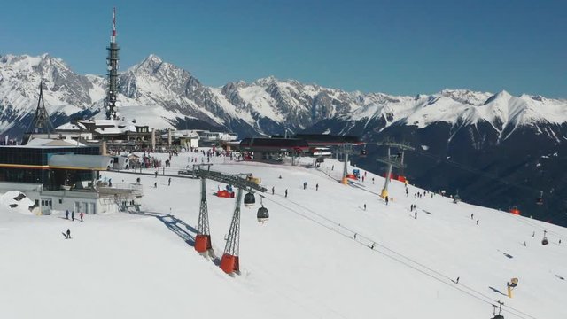 Aerial view of the Kronplatz skiing resort in South Tirol, Italy. Ski lifts moving, casting shadows on the snow, scores of skiers on the slopes enjoying sunny winter day. The sky is clear and blue.