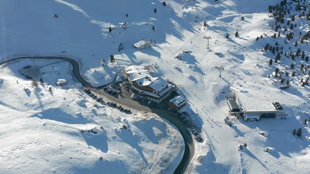 Aerial view of the Passo Gardena, in the Dolomites of the South Tyrol in northeast Italy. The road is meandering between the snow-covered hills. Many skiers are on the slopes, enjoying a lovely day.