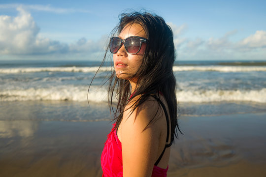 young beautiful and happy Asian Korean woman wearing sarong and sunglasses at the beach walking by the sea relaxed smiling cheerful enjoying Summer holiday