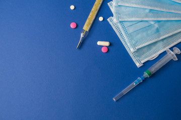 Thermometer, pills, tablets, masks and syringe on royal blue background.