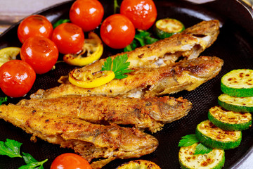 Fried whole fish with vegetable on black skillet. Close up.