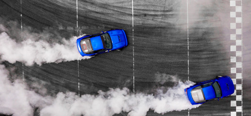 Aerial top view two cars drifting battle on asphalt race track with lots of smoke from burning...