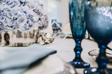 festive tables in the banquet room are decorated with compositions of white and blue flowers, on the tables are plates with napkins, glasses, candles, a wedding dinner