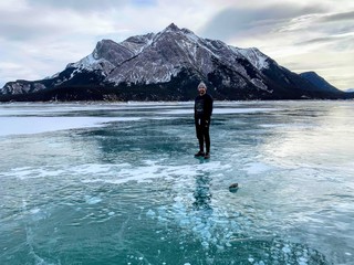 A young man smiling standing on the middle of a frozen lake with a mountain in the background on Abraham Lake, in the Canadian Rockies in Alberta, Canada