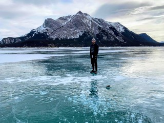 A young man smiling standing on the middle of a frozen lake with a mountain in the background on...