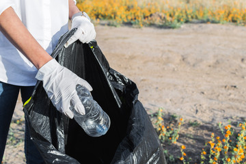 Woman in white globes puting plastic bottle in trash bag