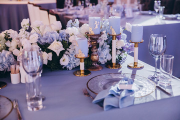 the festive table at the wedding party is decorated with flower arrangements, on the table are plates with napkins, glasses, candles, cutlery