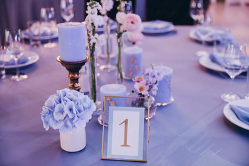 the festive table at the wedding party is decorated with flower arrangements, on the table are plates with napkins, glasses, candles, cutlery