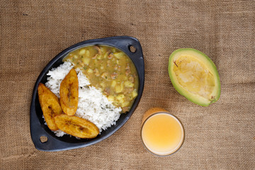 Above view of an artisanal mud dish containing meat hash soup with rice and slices of fried plantains and an avocado and Tamarillo juice on a jute mat