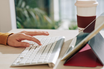 Close-up image of businesswoman working at her office desk and pushing button on tablet keyboard to...