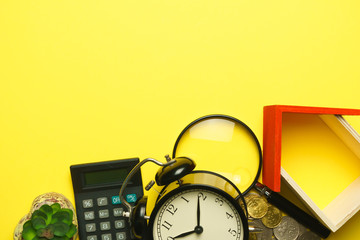 home replica with glass magnifying, coins, calculator and alarm clock on yellow background. copy space. flat lay