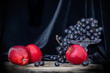 Still life of red apples and black grapes on a wooden surface on a black background