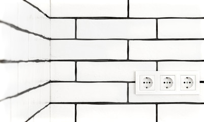 Electrical outlets against a white brick wall.