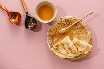 Delicious homemade pancakes with honey on a gently pink background. Top view, close-up. Traditional holiday celebration concept. Russian translation wide and happy Shrovetide Maslenitsa.