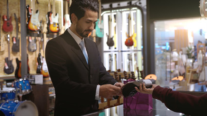 An upwardly mobile Middle Eastern man using a mobile phone - smartwatch to purchase product at the point of sale terminal in a retail store with nfc identification payment for verification