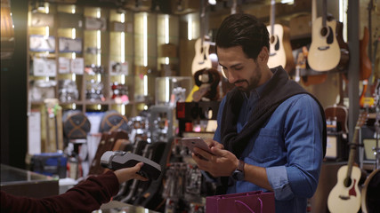An upwardly mobile Middle Eastern man using a mobile phone - smartwatch to purchase product at the point of sale terminal in a retail store with nfc identification payment for verification