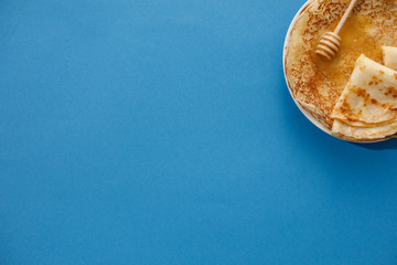 Tasty homemade pancakes with honey on a blue background. Top view, close-up. Traditional holiday celebration concept. Russian translation wide and happy Shrovetide Maslenitsa.