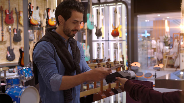 An upwardly mobile Middle Eastern man using a mobile phone - smartwatch to purchase product at the point of sale terminal in a retail store with nfc identification payment for verification