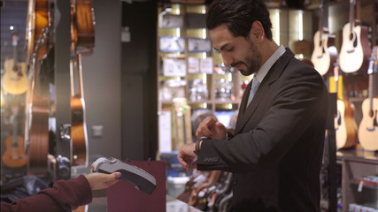 An upwardly mobile Middle Eastern man using a mobile phone - smartwatch to purchase product at the point of sale terminal in a retail store with nfc identification payment for verification