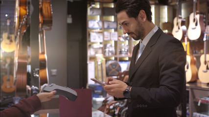 An upwardly mobile Middle Eastern man using a mobile phone - smartwatch to purchase product at the point of sale terminal in a retail store with nfc identification payment for verification