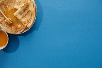 Tasty homemade pancakes with honey on a blue background. Top view, close-up. Traditional holiday celebration concept. Russian translation wide and happy Shrovetide Maslenitsa.