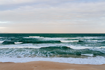 Fototapeta na wymiar Empty long beach with a beautiful sea view. White foam from a sea wave