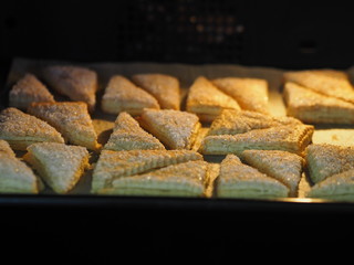 Homemade puff pastry for shortbread Triangle on a black baking sheet in the oven. Sprinkled with sugar and white sesame seeds. Holiday.