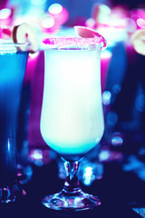 Blurred glass of pink and blue neon cocktails and milkshakes with sugar rims on bar background, party concept with copy space. Selective soft focus