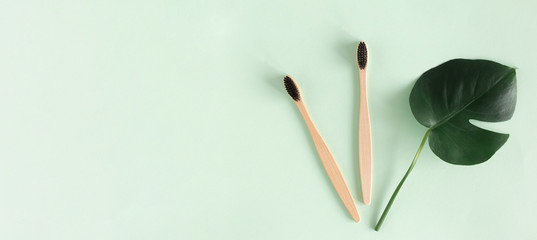 Zero waste concept. Top view natural eco bamboo toothbrush with monstera leaves on green background Copy space