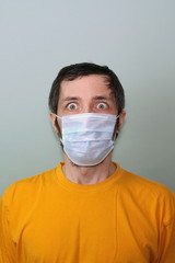 Middle-aged adult man in a yellow T-shirt on a gray background in a medical mask with bulging eyes. Coronavirus Disease Outbreak Protection from China
