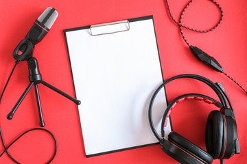 Headphones, microphone and clipboard with white paper on red background. Concept music or podcast. Top view, flat lay Copy space Mockup for your text
