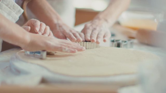 Close up woman and girl hands cutting dough with cookie cutters on kitchen table