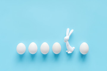 Row white eggs and bunny rabbit figurine on blue background with copy space. Happy easter, Not like everyone else concept. Creative Flat lay Top view. Template for greeting card, invitation, postcard