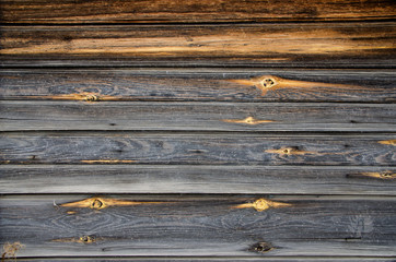Battered, faded old gray-yellow horizontal unpainted wooden planks with splotches of knots. Wooden...