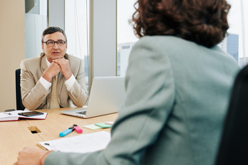 Pensive mature entrepreneur listening to his female colleague explaining her innovative ideas