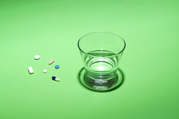 Glass of water and vitamins, pills and tablets on green background with copy space